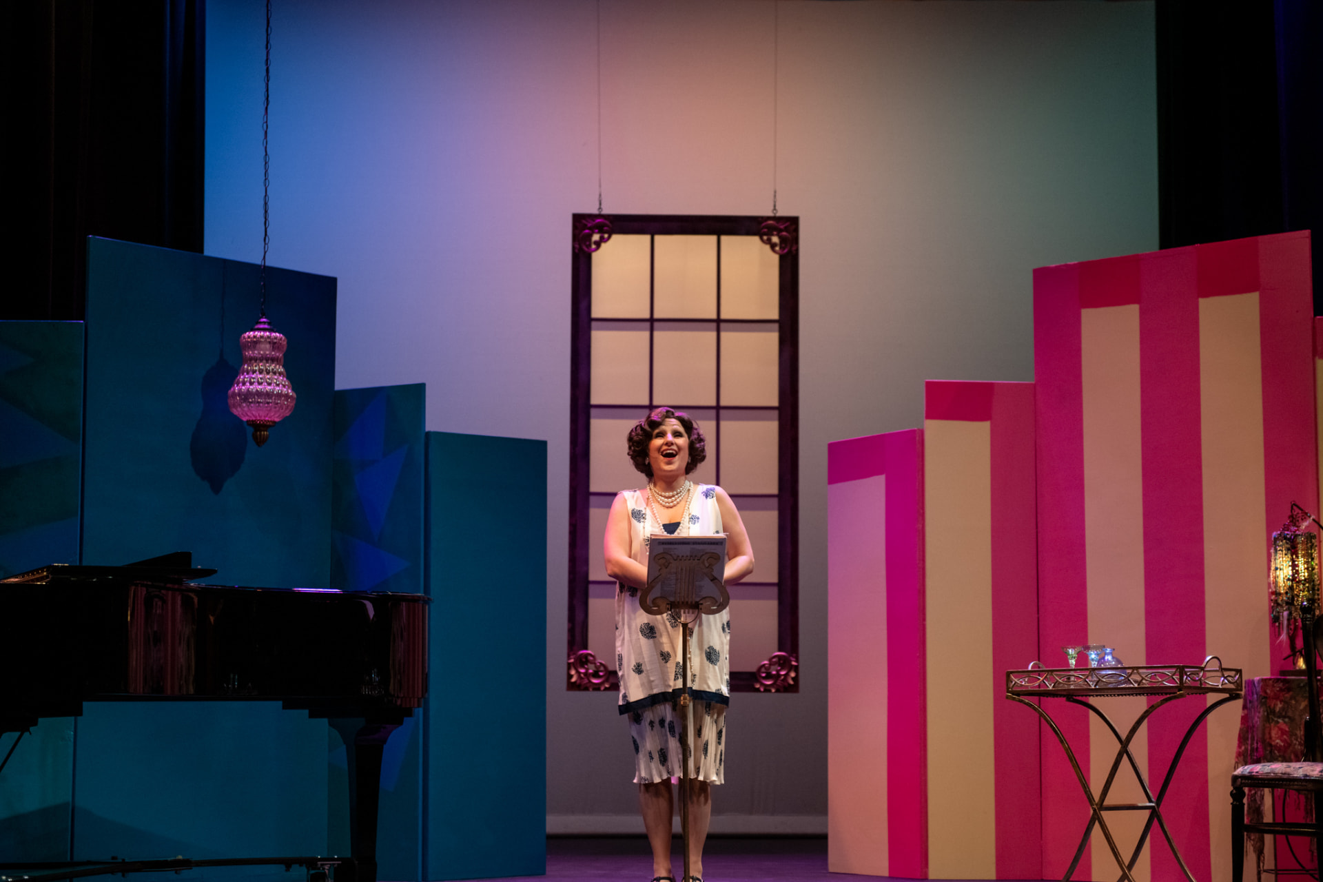 Singer at a music stand between a grand piano and a pink-striped flat