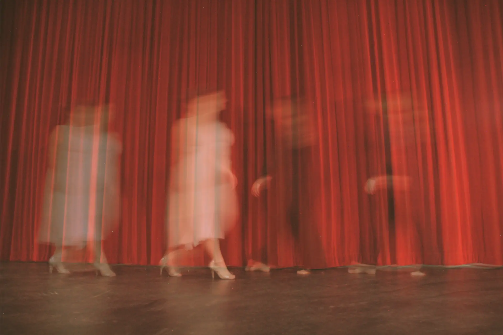Four performers walking across a stage in front of a red curtain, captured with motion blur